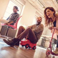 Adults playing on scooters in an office