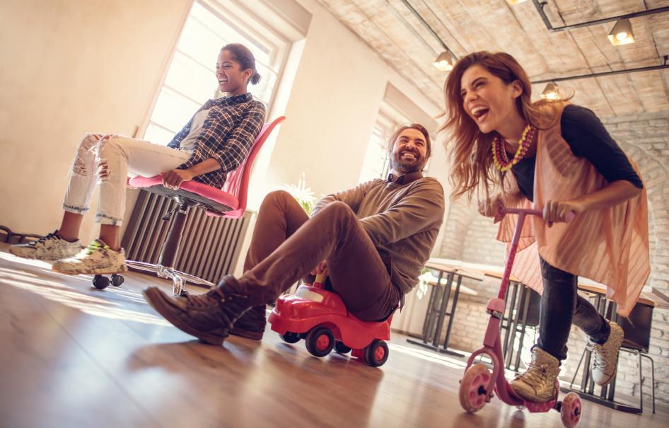 Adults playing on scooters in an office